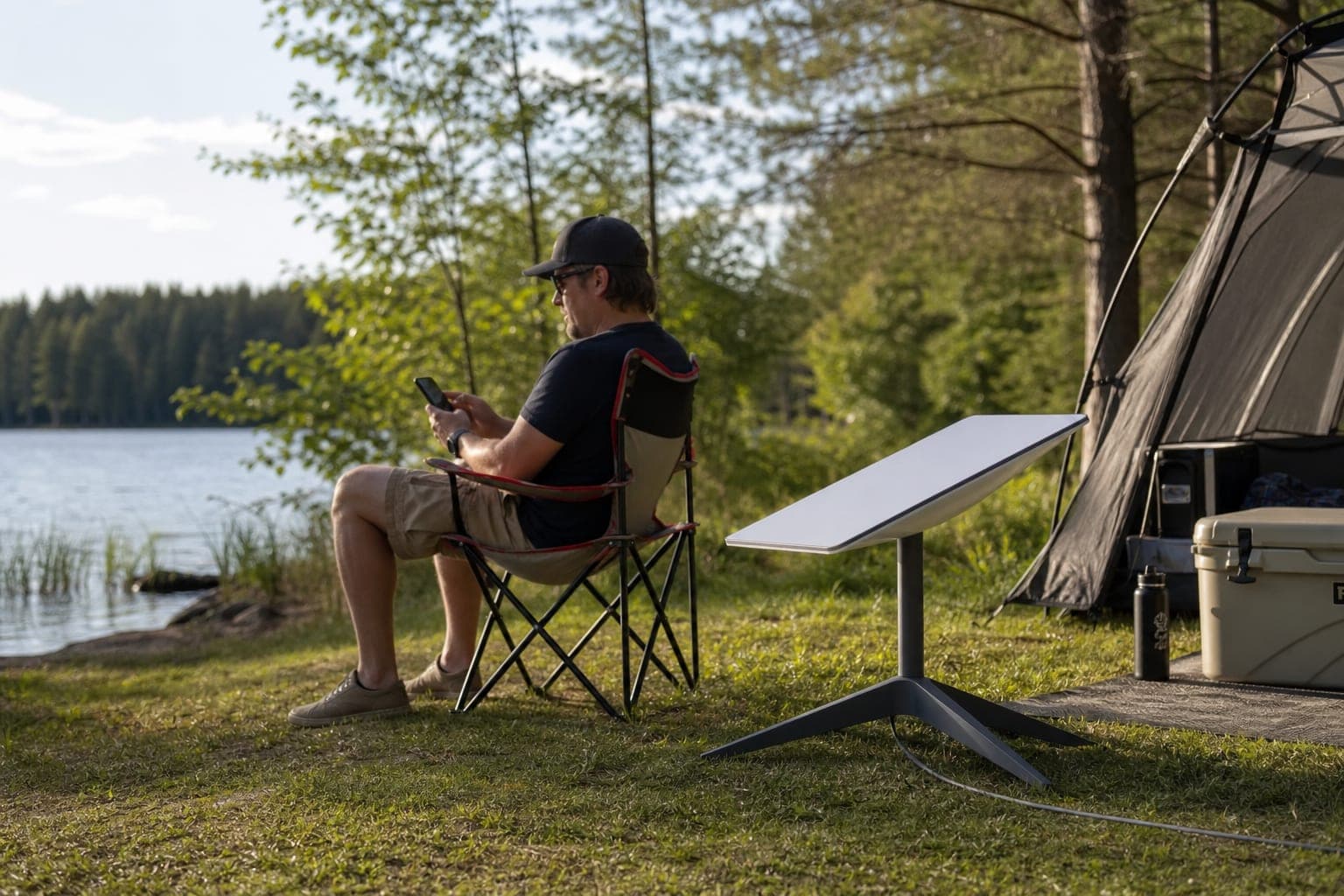 Person using a phone near a Starlink Gen2 dish on an included ground stand