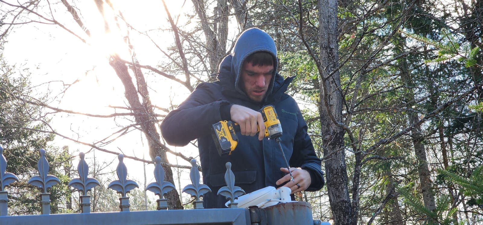 McKee technician mounting a security camera on a gate post at a wooded property